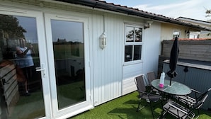 A patio with artificial grass, a table with chairs, and a sliding glass door. - Seaside Chalet Escape in Bridlington (Bridlington)