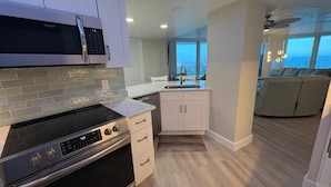 A modern kitchen with a built-in oven, microwave, and white cabinetry. There is a large window providing a view of the cityscape. - 24th Floor OceanView Oasis (Daytona Beach Shores)