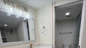 A modern bathroom with a marble countertop, a large mirror, a towel ring, and a shower area. - 24th Floor OceanView Oasis (Daytona Beach Shores)