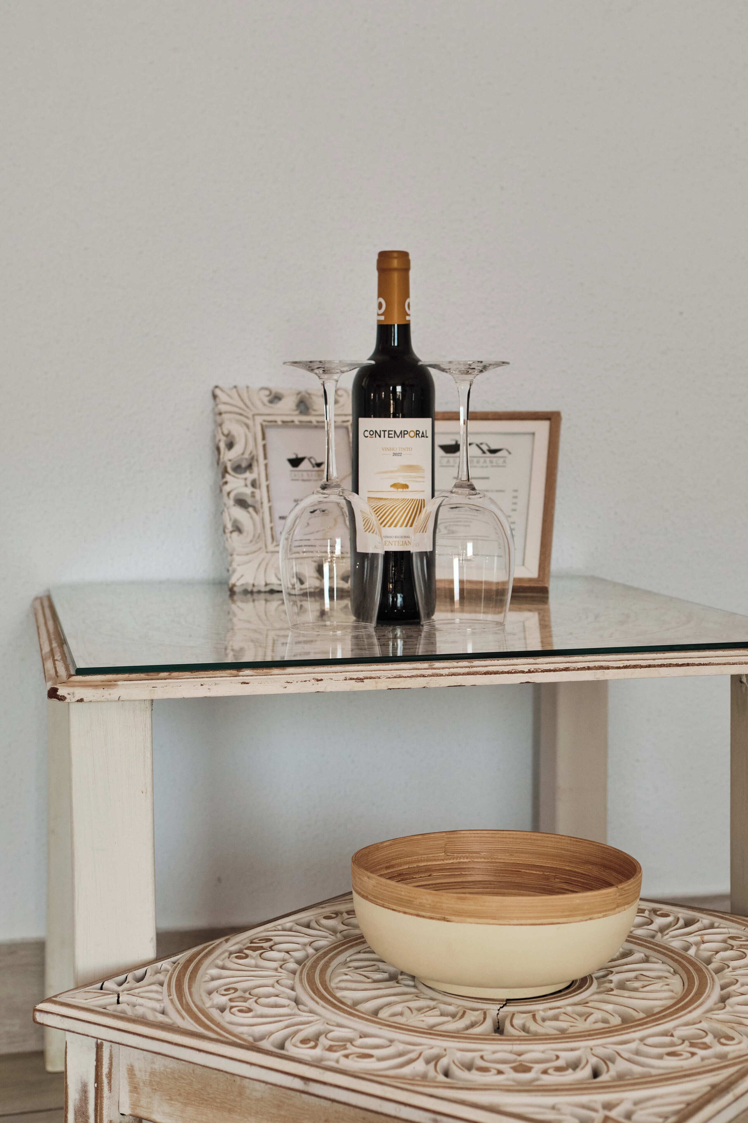 Een tafel met een fles wijn, twee wijnglazen en een decoratieve schaal.