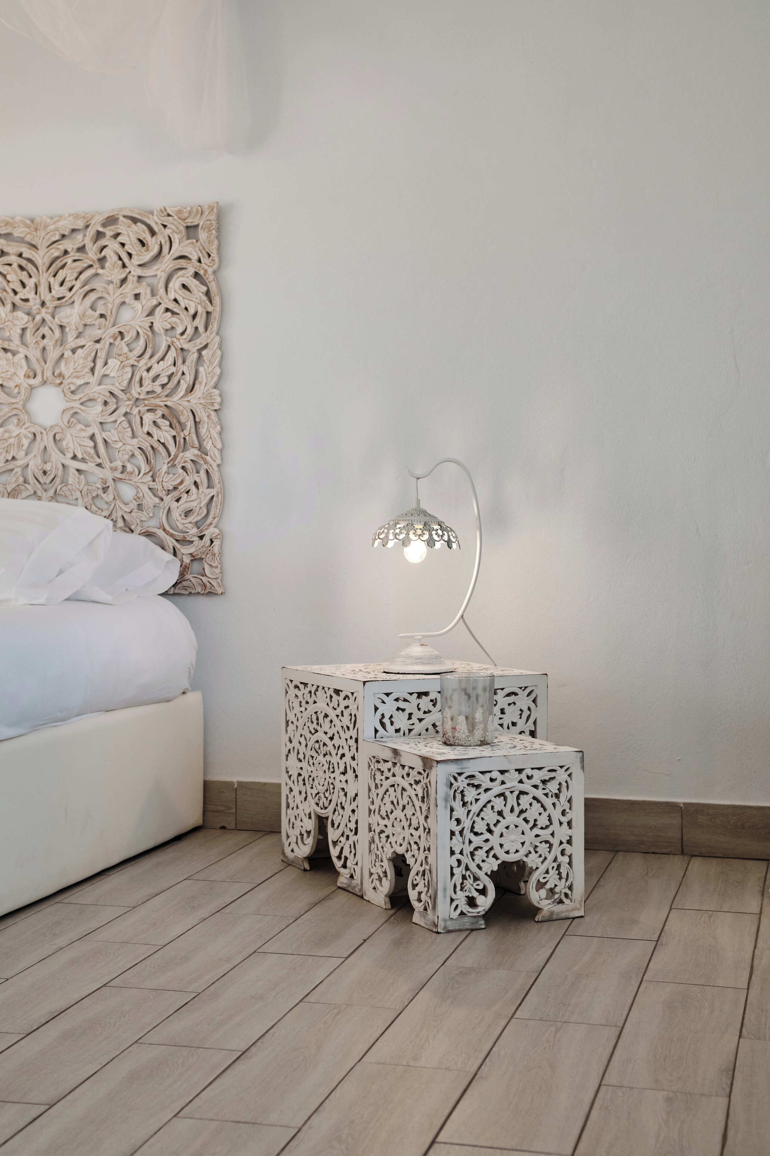 A bedroom with a bed, a decorative wall piece, and a nightstand with a lamp.