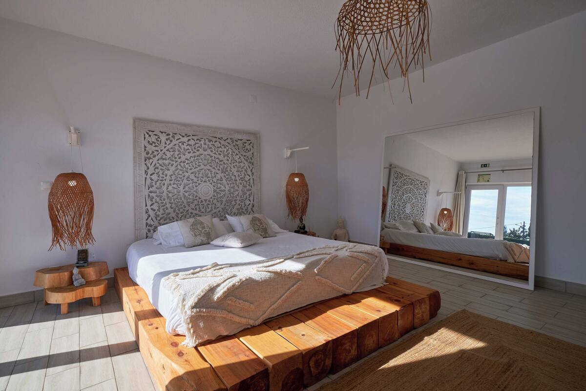 Une chambre avec un grand lit, une plateforme en bois et un grand miroir qui reflète la pièce.