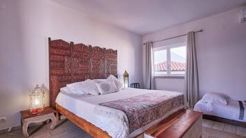 A bedroom with a wooden headboard, a bed with white linens, a nightstand with a lamp, and a window with curtains.