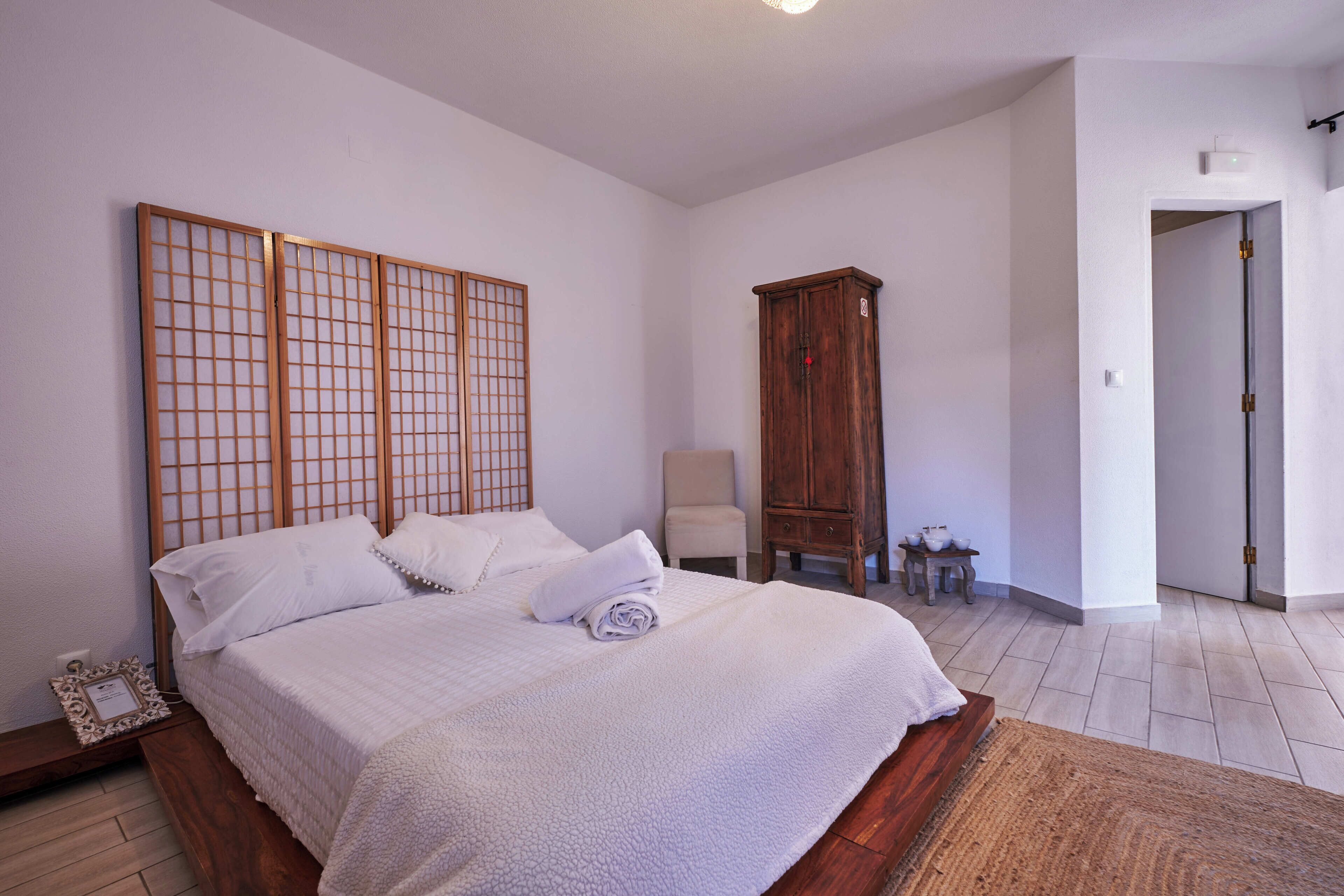 Une chambre avec un grand lit, une armoire en bois et une chaise.