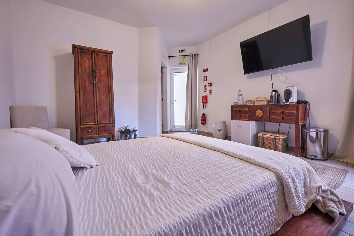 Une chambre comprenant un lit, une armoire en bois, une télévision et un petit coin cuisine.