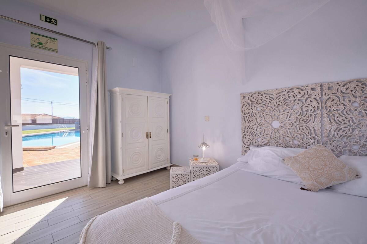 Une chambre à coucher comprenant un lit, une table de chevet, une armoire et une vue sur une piscine, visible à travers une porte vitrée.