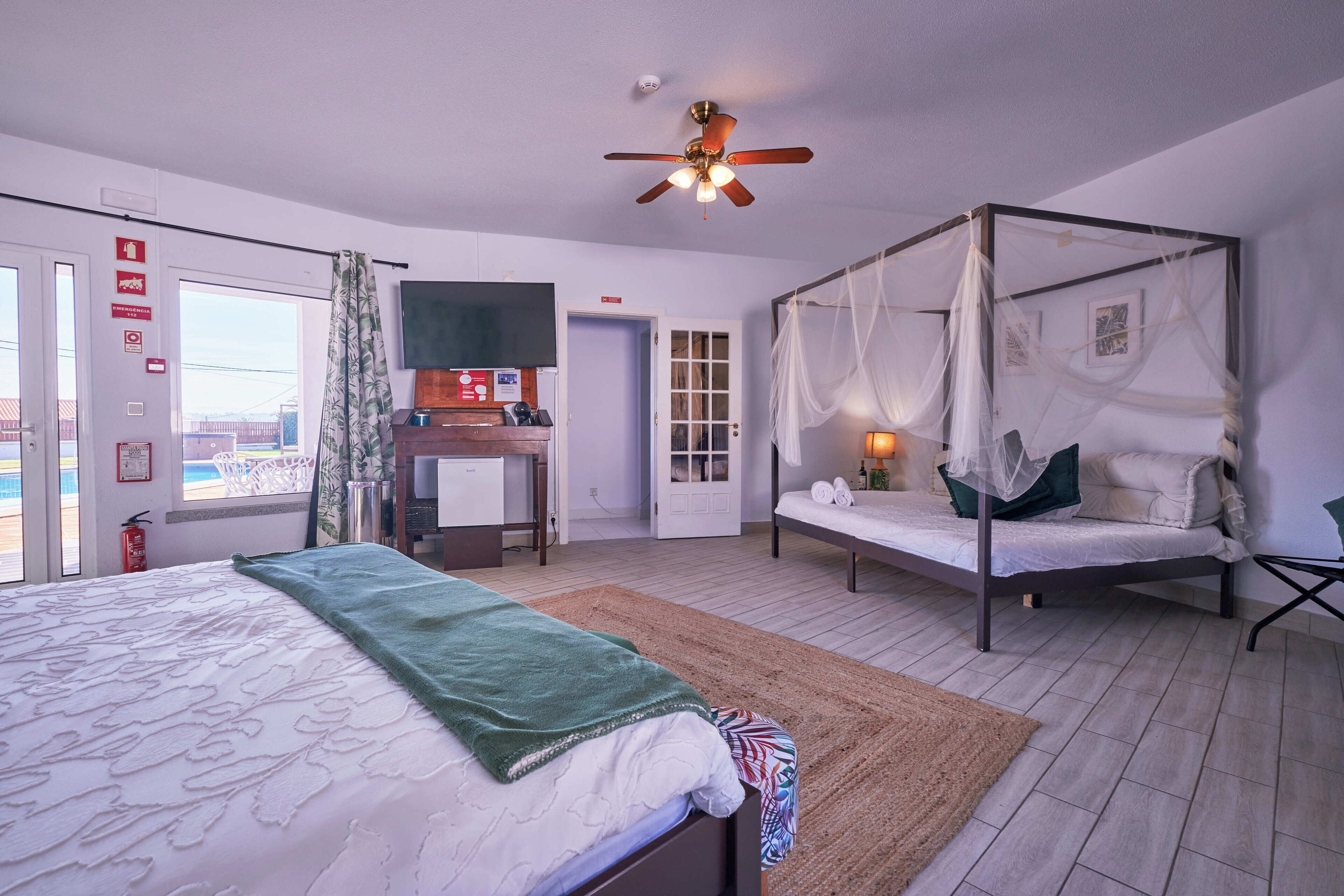 A bedroom with a large bed, a canopy bed, a desk, and a view of the beach.