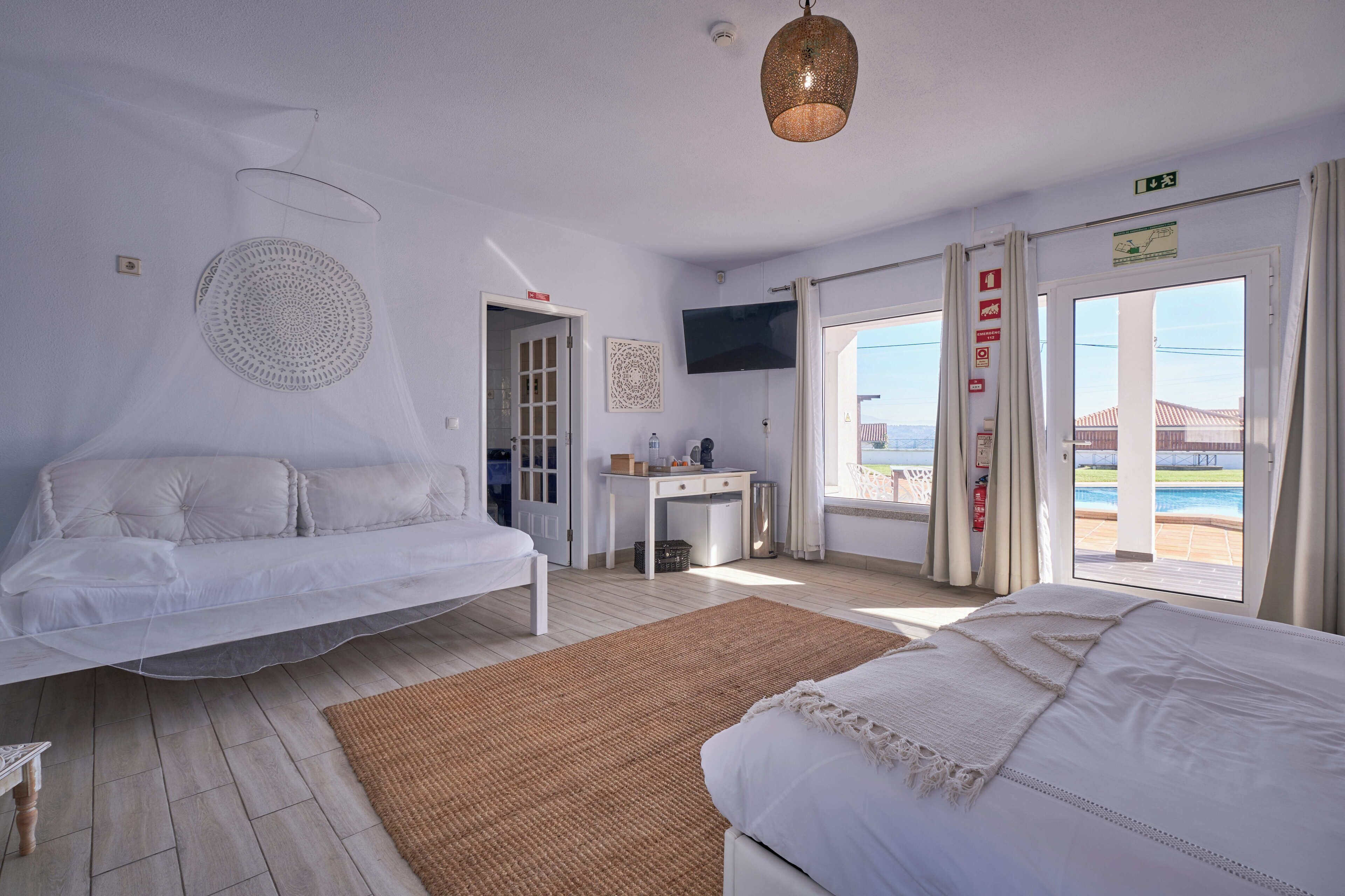A hotel room with a bed, a desk, a TV, and a view of the pool.