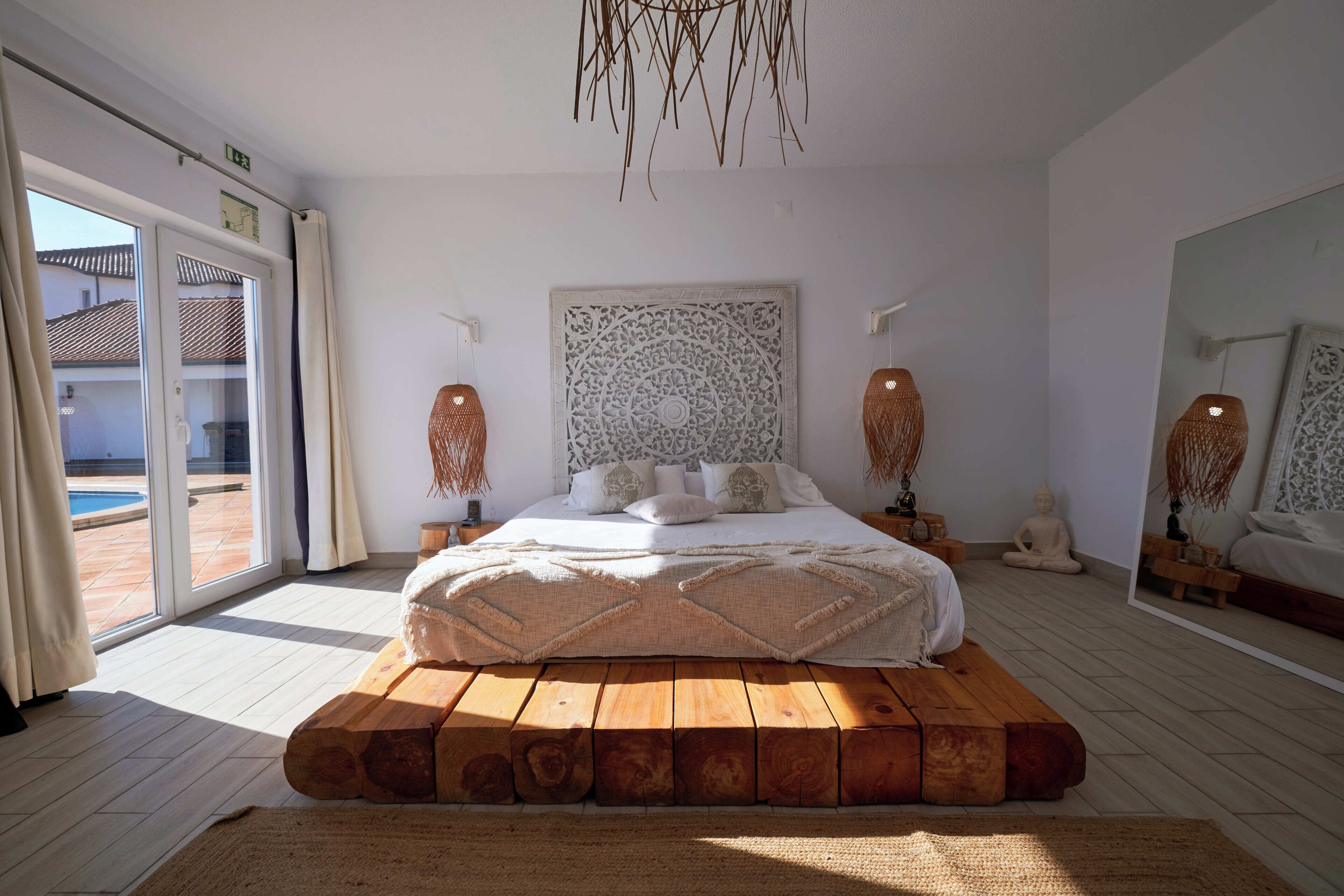 Un dormitorio con una cama grande, una plataforma de madera, un tapiz decorativo y una estatua de Buda.