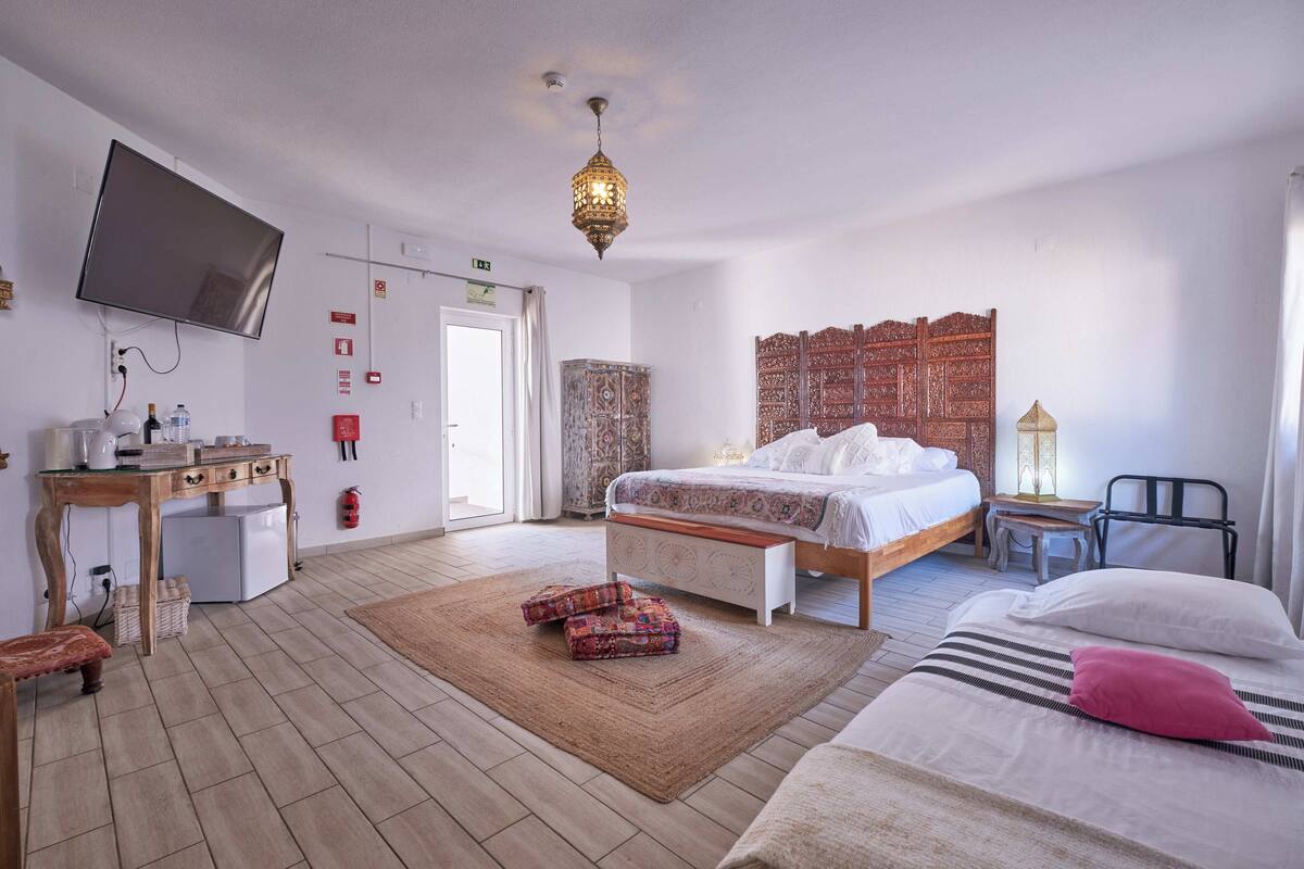 Une chambre d’hôtel comprenant un lit, une table de chevet, un bureau avec une chaise, un téléviseur fixé au mur et une tapisserie à motifs ornant le mur.