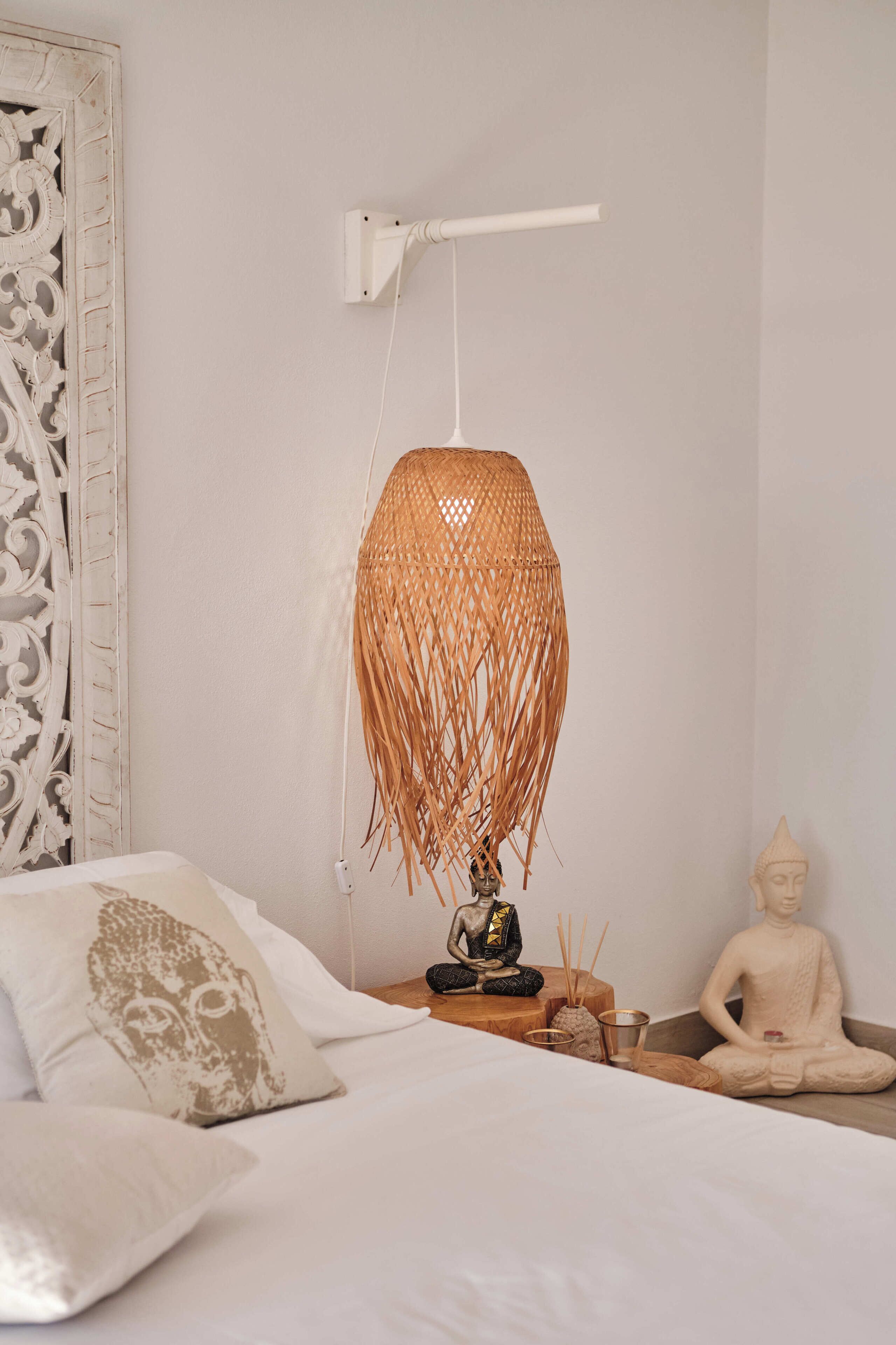 Un dormitorio con una cama, una lámpara de pared, una estatua de Buda y un panel decorativo.