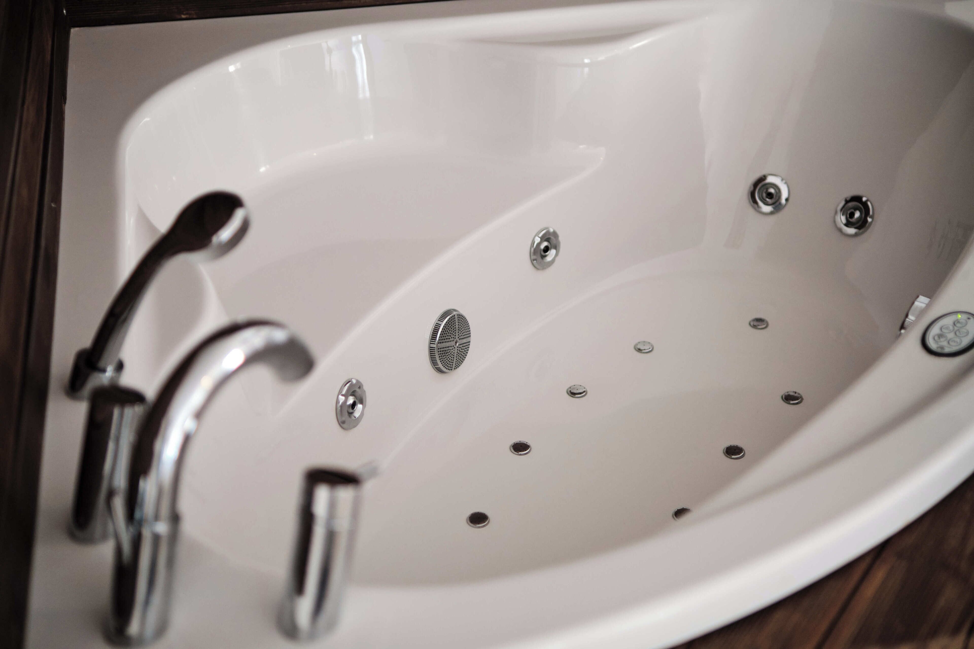 Eine weiße Badewanne mit zwei Chromarmaturen und einem Abfluss.