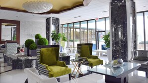 A modern lobby with a marble reception desk, green armchairs, and a chandelier. - 2bd2bth Partial Ocean view Ste w/ balcony, Pool, nearby dining, beach access (Miami Beach)