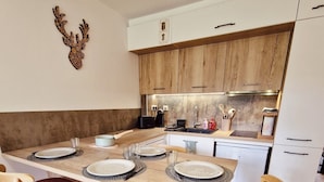A modern kitchen with wooden cabinets, a central island, and a dining area with four chairs. - Studio Hart 2 (Les Gets)