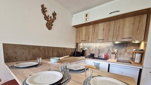 A modern kitchen with wooden cabinets, a built-in oven, and a dining area set with plates and cutlery. - Studio Hart 2 (Les Gets)