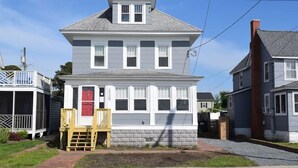 A two-story house with a red door, a small porch, and a brick foundation. - Island Time- 3BR Home | Water View Chincoteague Bay (Chincoteague)