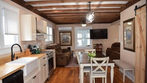 A compact kitchen with white cabinets, a wooden countertop, and a dining area with a table and chairs. - Island Time- 3BR Home | Water View Chincoteague Bay (Chincoteague)