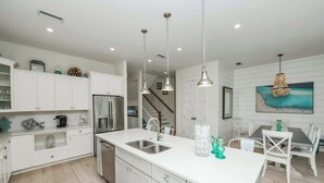 A modern kitchen with white cabinetry, stainless steel appliances, and pendant lighting. - Pineapple Paradise~WATER SLIDE/Heated Pool & Spa! (Holmes Beach)