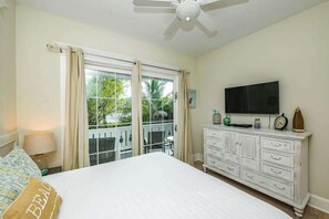 Una camera da letto con un letto, una TV, una cassettiera e un balcone vista alberi.