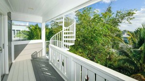 A covered outdoor area with a white spiral staircase leading to a balcony, surrounded by lush greenery. - Pineapple Paradise~WATER SLIDE/Heated Pool & Spa! (Holmes Beach)