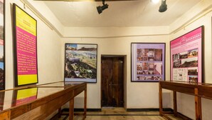 Un pasillo con bancos de madera, carteles informativos enmarcados y una puerta de madera.