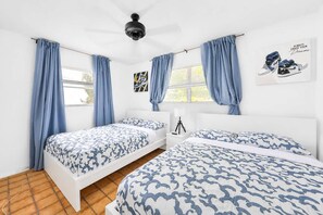A bedroom with two beds, a ceiling fan, and a window with curtains. - Villa Chill on the Hill (Hollywood)