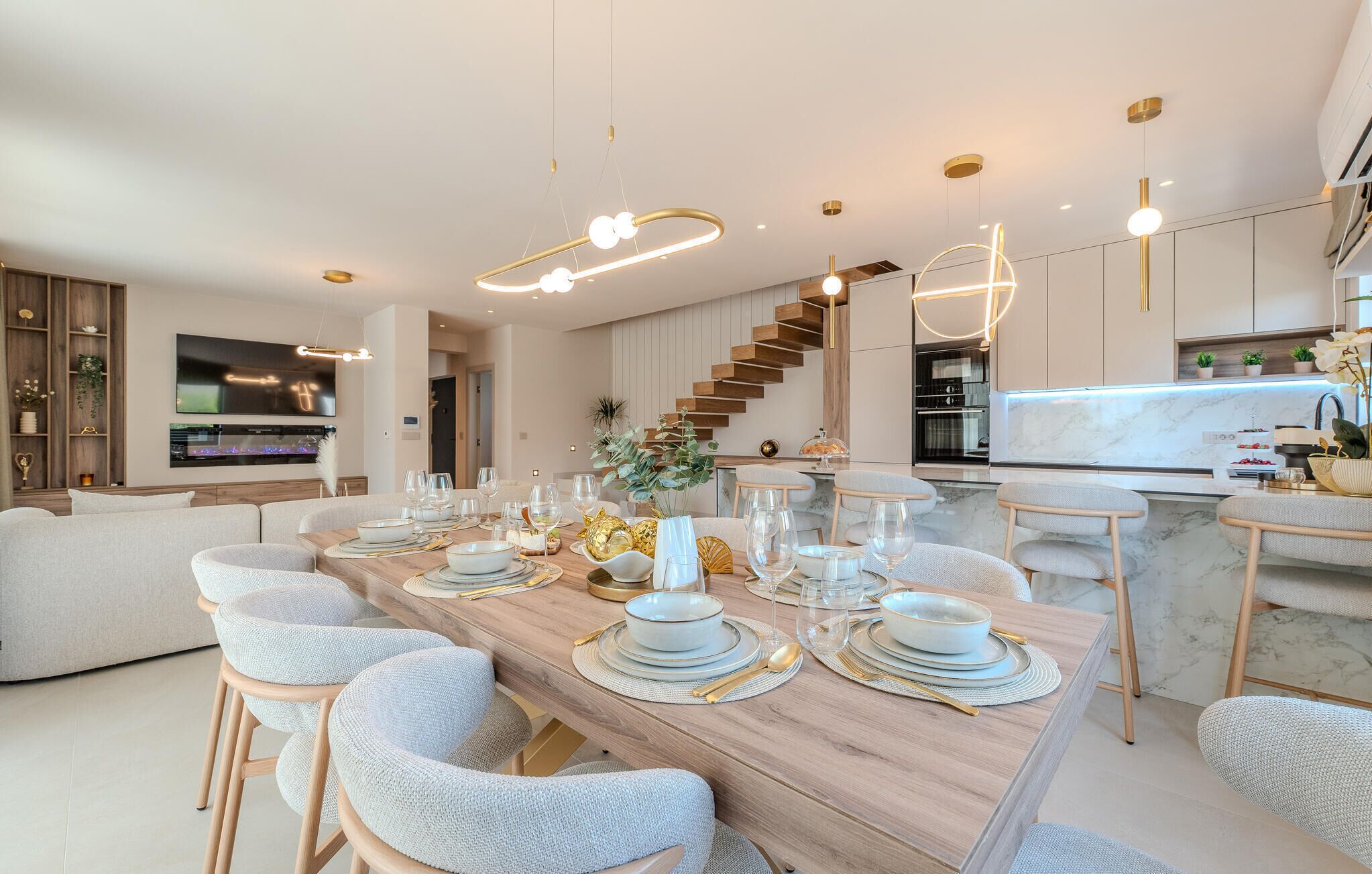 Un espace repas moderne avec une table en bois dressée pour six personnes, entourée de chaises rembourrées. Un escalier est visible au fond, menant à un niveau supérieur.