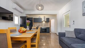 Una sala de estar moderna con un sofá gris, una mesa de comedor de madera con sillas y una cocina con armarios grises y un horno empotrado.