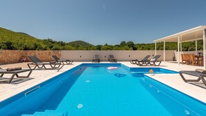 Una piscina rectangular con agua azul cristalina, rodeada de sillas de descanso y una zona de estar cubierta.