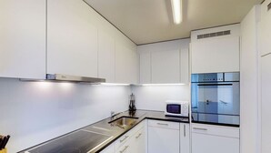 Een moderne keuken met witte kasten, een zwart aanrecht, een inbouwmagnetron en een roestvrijstalen afzuigkap.
