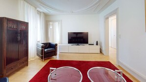 Een woonkamer met een televisie, een bank, een kast en een rood vloerkleed.