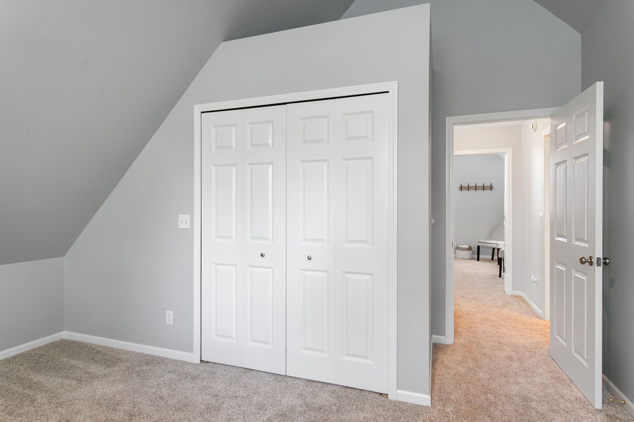 A room with a white door, a carpeted floor, and a sloped ceiling.