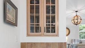Un salon avec une cheminée, un meuble en bois doté de portes en verre, un panier en osier et un tableau encadré accroché au mur.