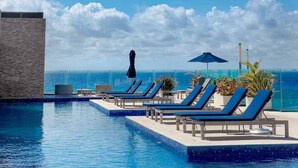 Zona de piscina con sillones reclinables y sombrillas, con vista al océano.