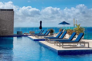 A poolside area with lounge chairs and umbrellas, overlooking the ocean. - Newer Luxury 2BD Close to Ocean (Playa del Carmen)