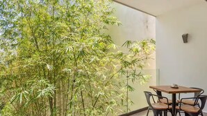 Ein modernes Zimmer mit großem Fenster und Blick auf Bambuspflanzen, einem runden Holztisch mit vier Stühlen sowie einer kleinen Wandleuchte.