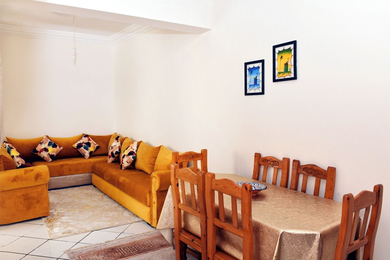 A living room with a sofa, a dining table with chairs, and two framed pictures on the wall.