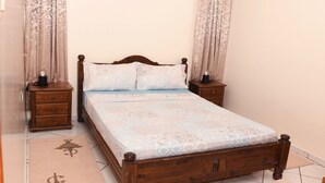 A wooden bed with a patterned bedspread, two nightstands, and curtains. - Your cozy home in Agadir - discover comfort and tradition (Agadir)
