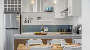 A modern kitchen with a stainless steel refrigerator, a wooden dining table set for four, and a blue toaster on the countertop.