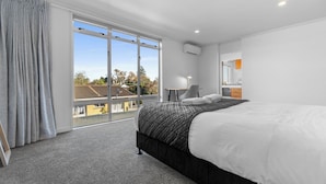 A modern hotel room with a large bed, a desk, and a view of the neighborhood.