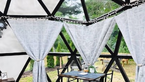 Une tente équipée d’un lit, d’une table et de chaises, avec vue sur la verdure environnante.