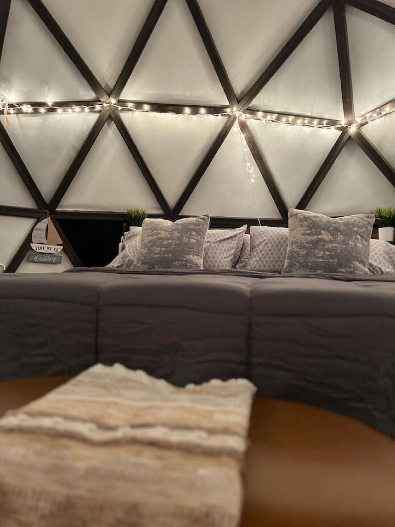 A bed with a geometric headboard, multiple pillows, and a bedside plant.