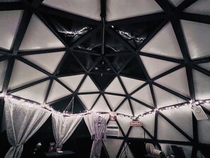 A geodesic dome structure with a central air conditioning unit, string lights, and a welcome sign.