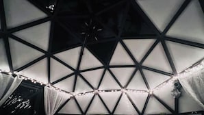 Une pièce dotée d’un plafond au design géométrique, d’un lit avec des oreillers et de guirlandes lumineuses.