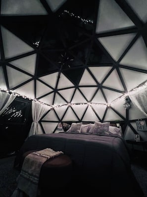 Una habitación con diseño geométrico en el techo, una cama con almohadas y luces de cadena.