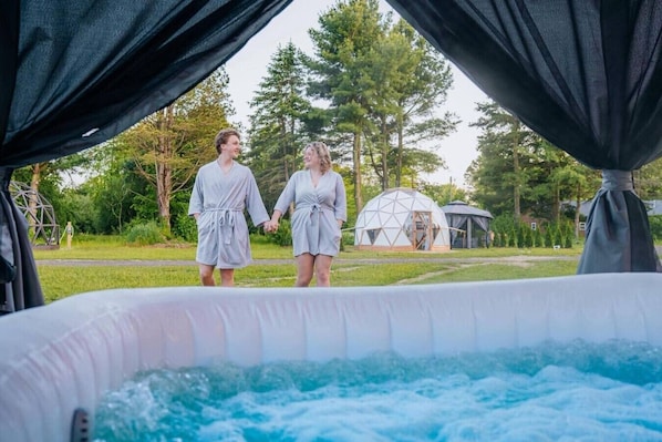 Two people holding hands in a garden with a hot tub and a geodesic dome structure.