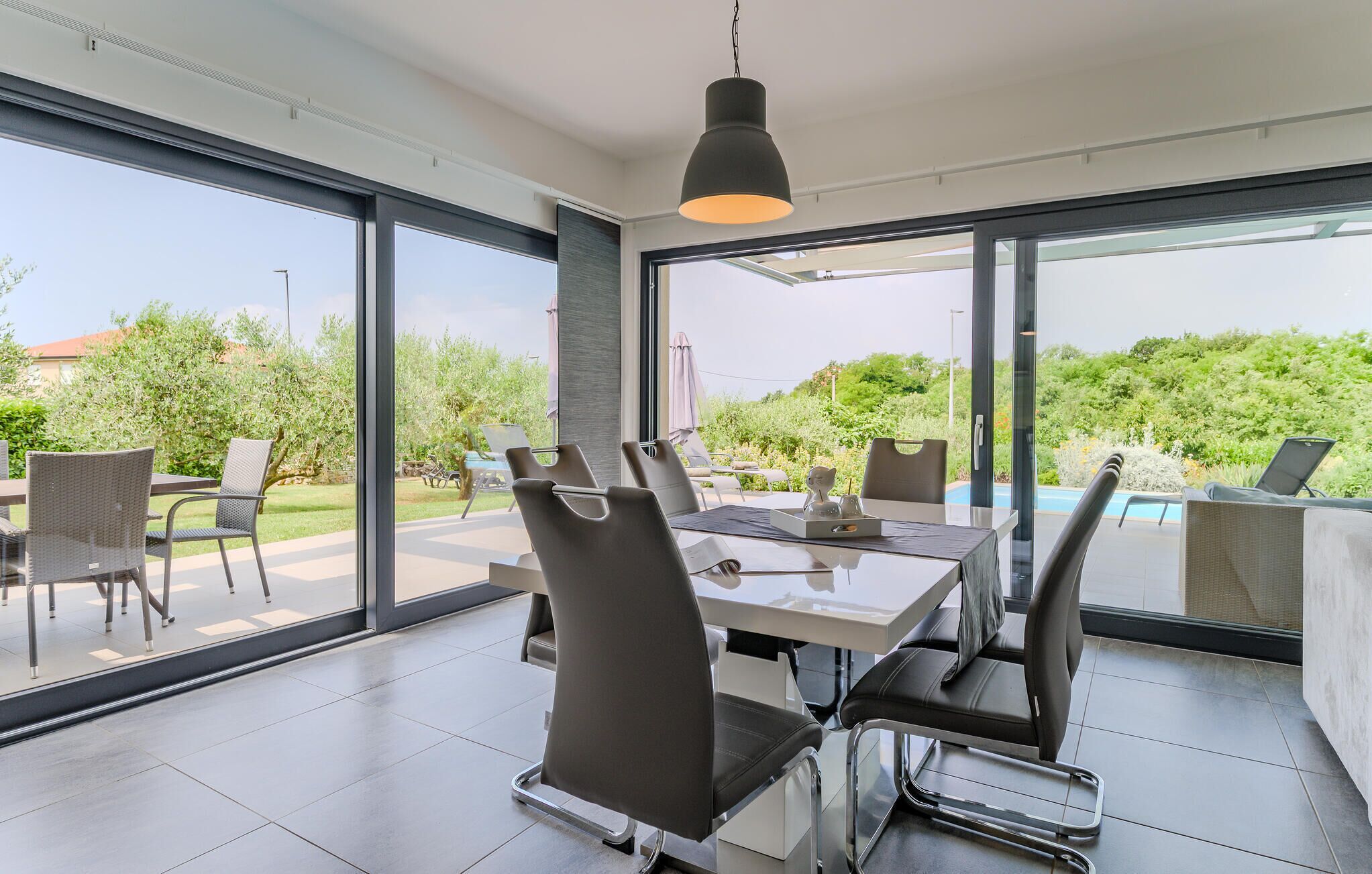Un espace repas moderne avec une table et des chaises en verre, de grandes fenêtres et une vue sur l’extérieur.