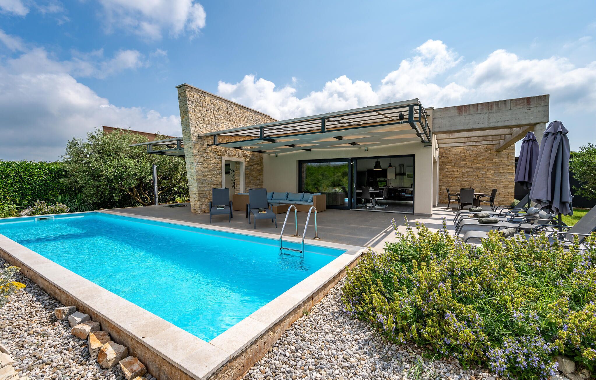 A modern outdoor pool area with a stone patio, lounge chairs, and a covered seating area.