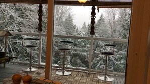 A covered outdoor area with a wooden floor, metal chairs, and a view of snow-covered trees. - Spacious 3 bedroom unit near the lake (Lindell Beach)