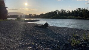 A riverbank with a rocky shore and a log in the foreground. - Spacious 3 bedroom unit near the lake (Lindell Beach)